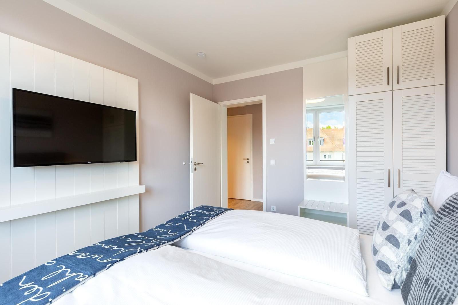 Schlafzimmer mit Bett, TV und Kleiderschrank. Blick auf Balkon und Dach.