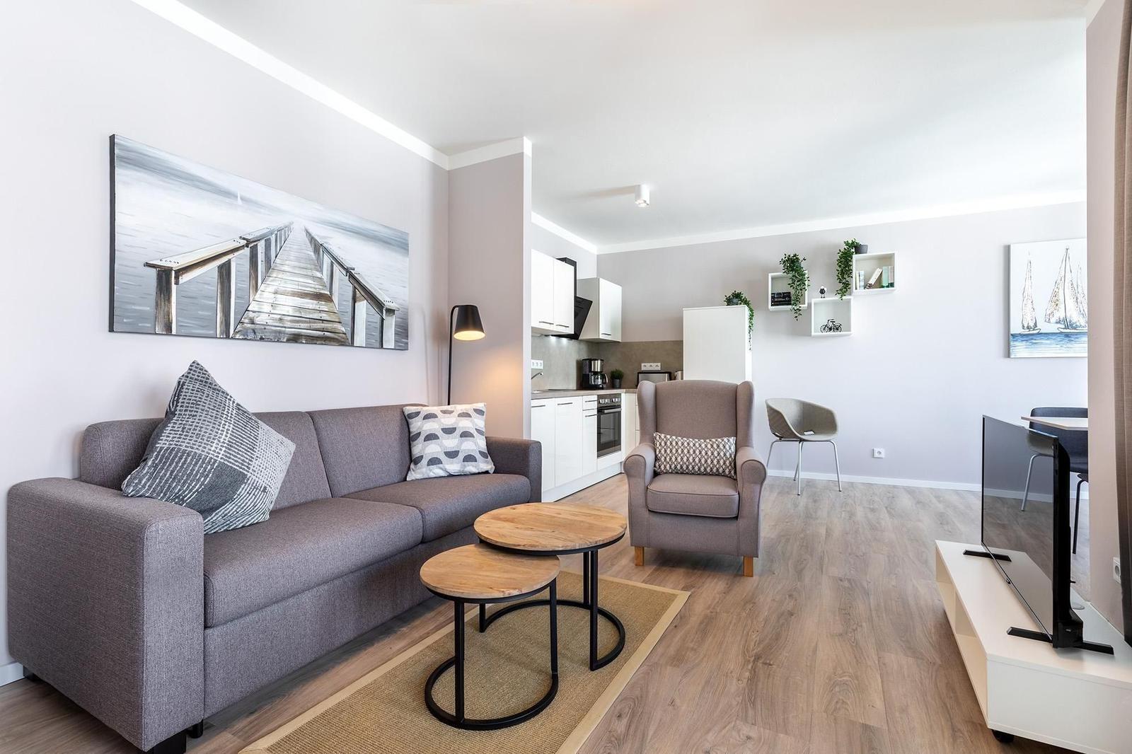 Wohnzimmer mit Sofa, Sessel und Küchenbereich. Holzboden und Wandbild.