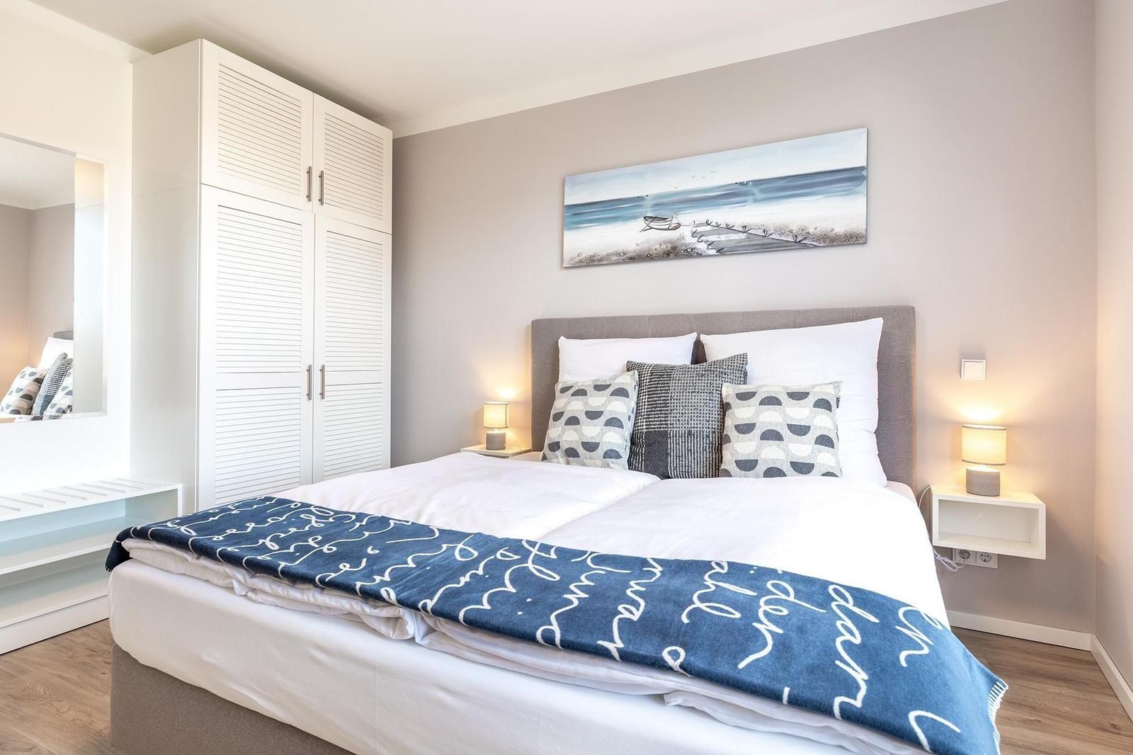 Schlafzimmer mit Doppelbett, Kleiderschrank und Wandbild.