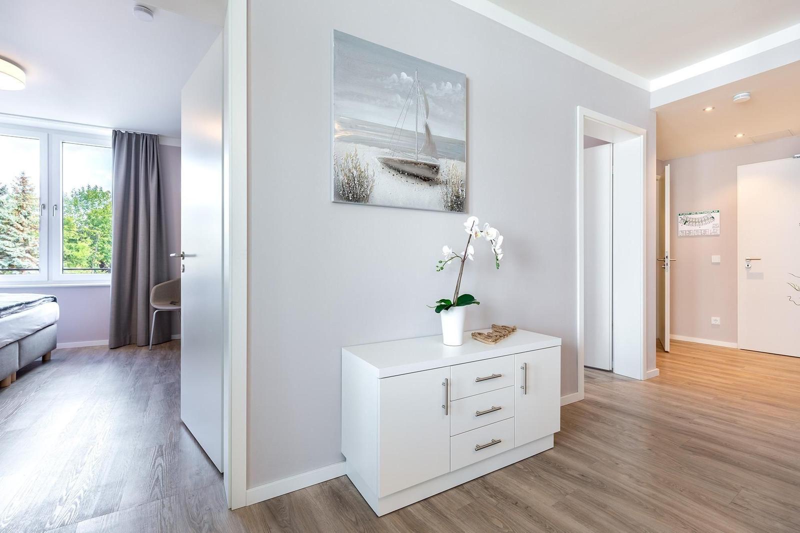 Flur mit Schrank, Wandbild und Pflanze. Tür führt in Schlafzimmer mit Fenster.