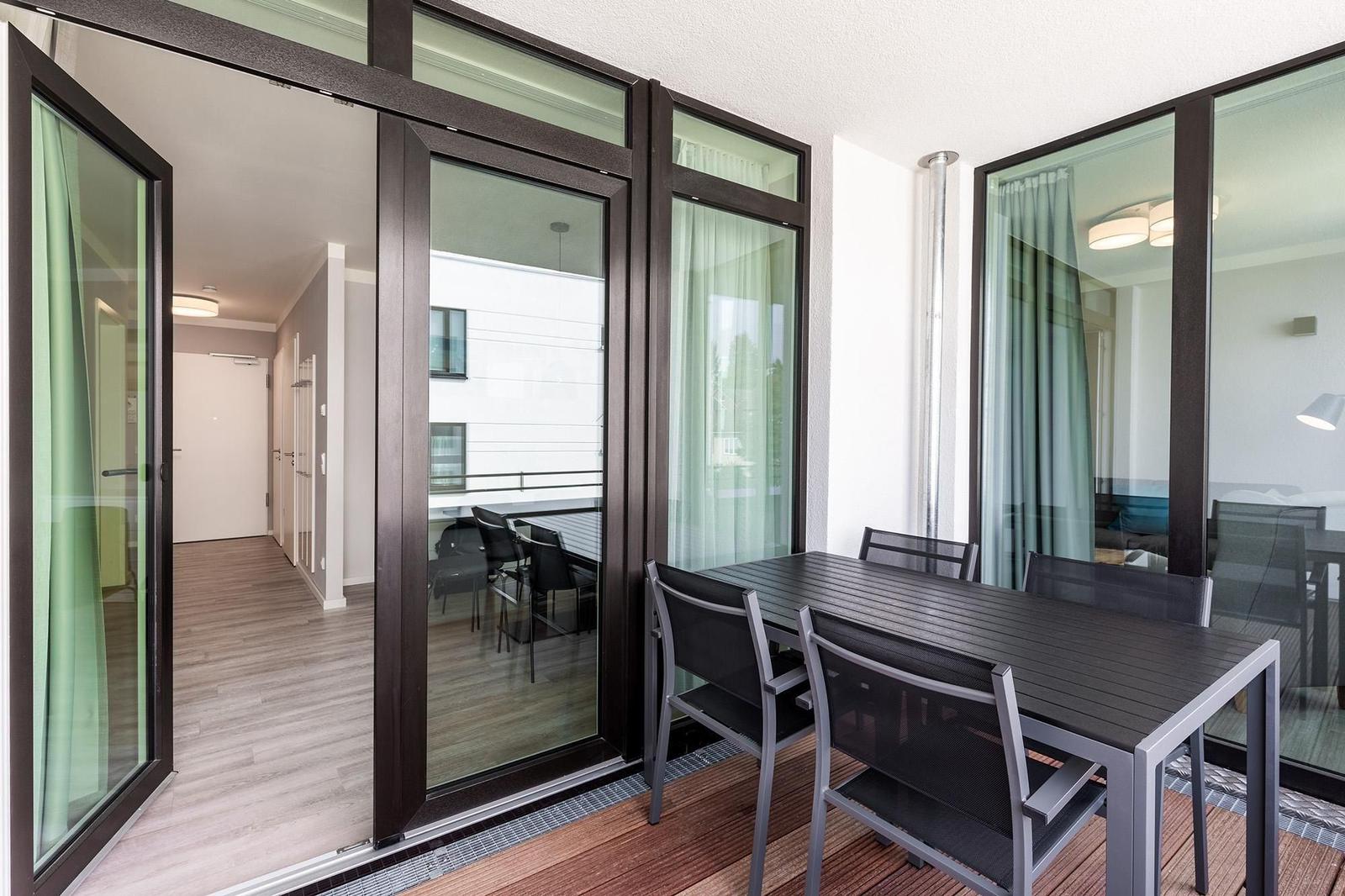 Terrasse mit Tisch und Stühlen, Zugang zum Innenraum über Schiebetüren.