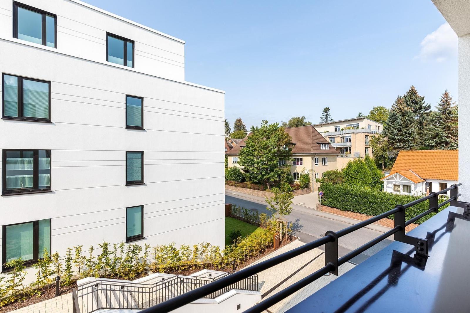 Blick von Balkon auf moderne Wohnanlage und grüne Umgebung mit Straßen und Häusern.