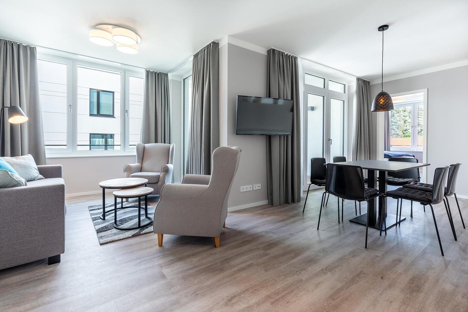 Wohn- und Essbereich mit Sofa, Sesseln, TV und Tisch mit Stühlen.