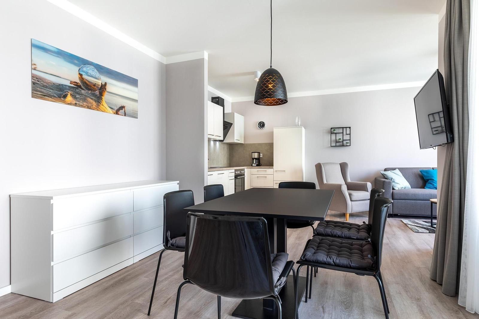 Essbereich mit Tisch und Stühlen, Küche und Wohnbereich mit Sofa und Fernseher.