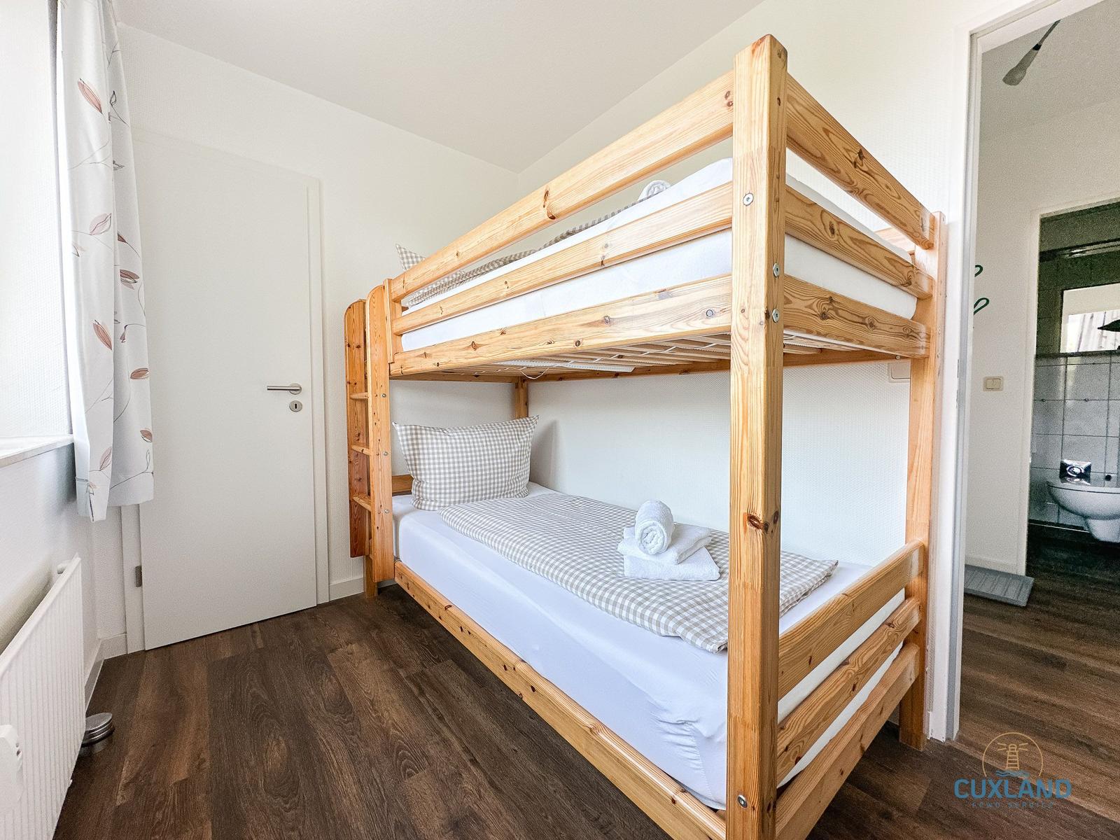 Zimmer mit Holz-Etagenbett, Fenster und Tür. Bad sichtbar.