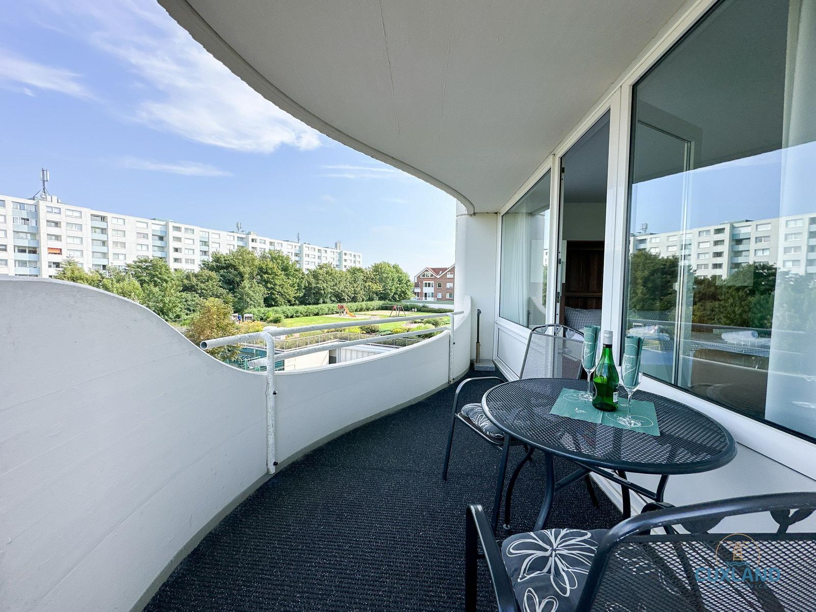 Terrasse mit Tisch, Stühlen und Blick auf Grünfläche und Gebäude.