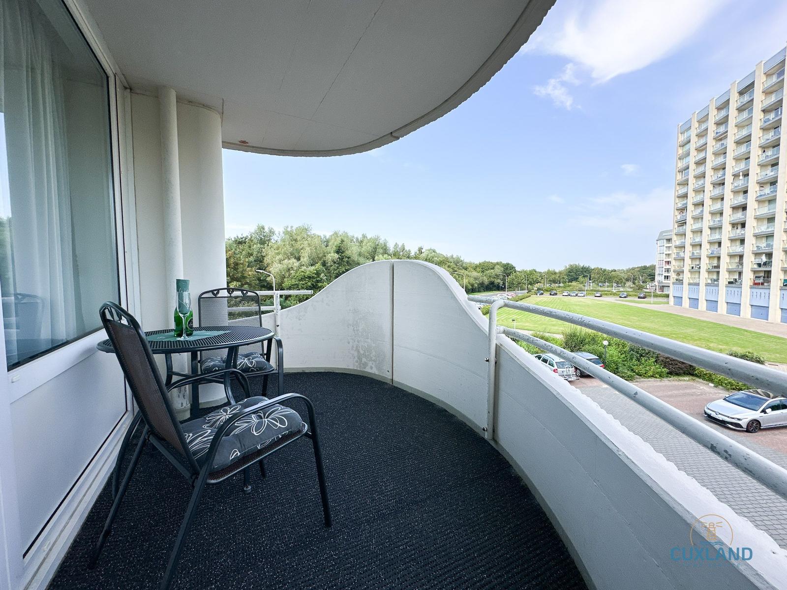 Terrasse mit Tisch und Stühlen, Blick auf Grünfläche und Hochhaus.