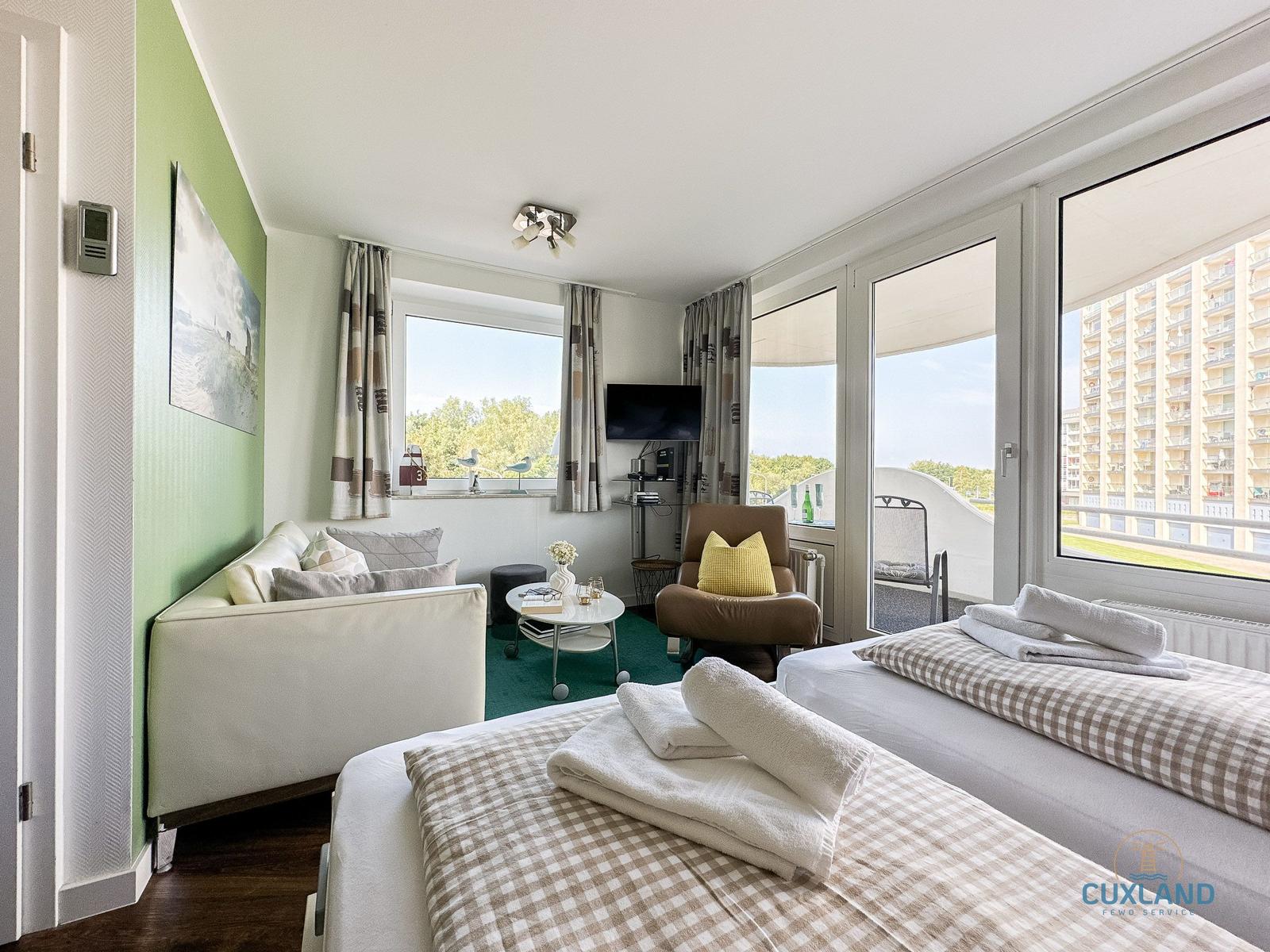 Zwei Betten, Sofa, TV und Balkon mit Blick auf Hochhäuser.