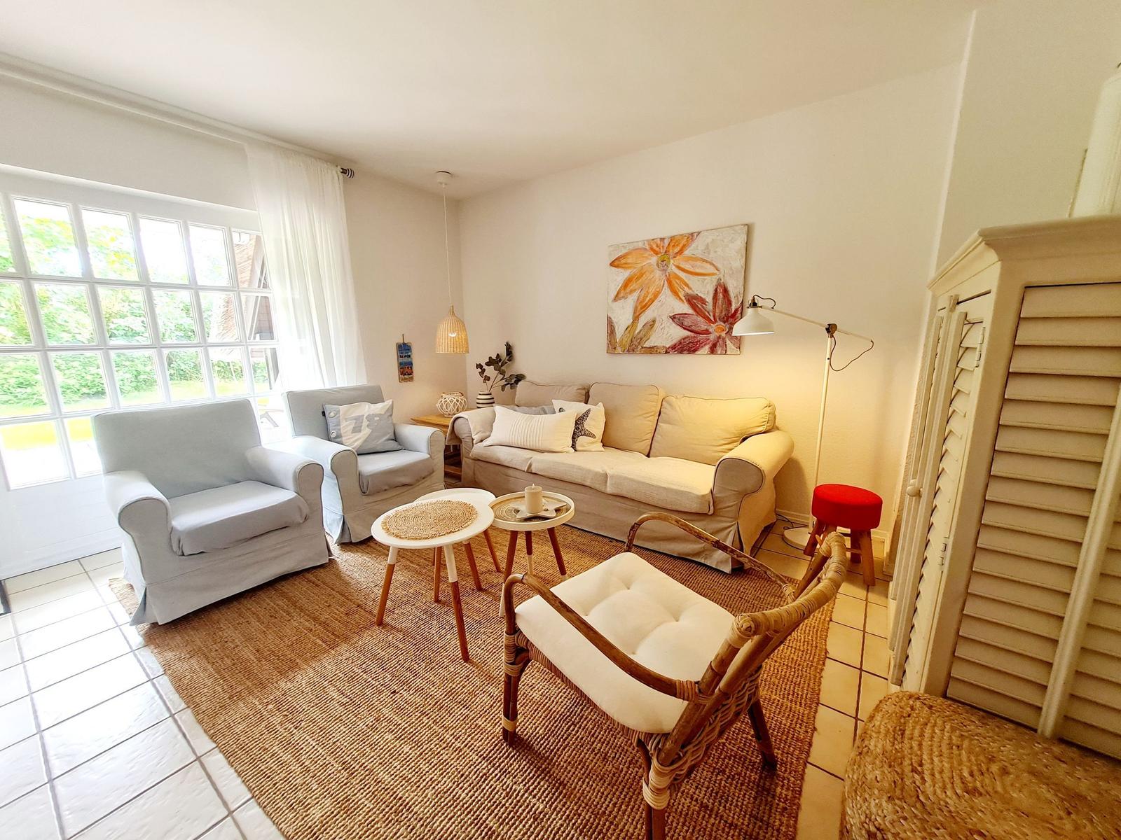 Wohnzimmer mit Sofa, Sesseln und Teppich. Wandbild und Fenster mit Blick nach draußen.