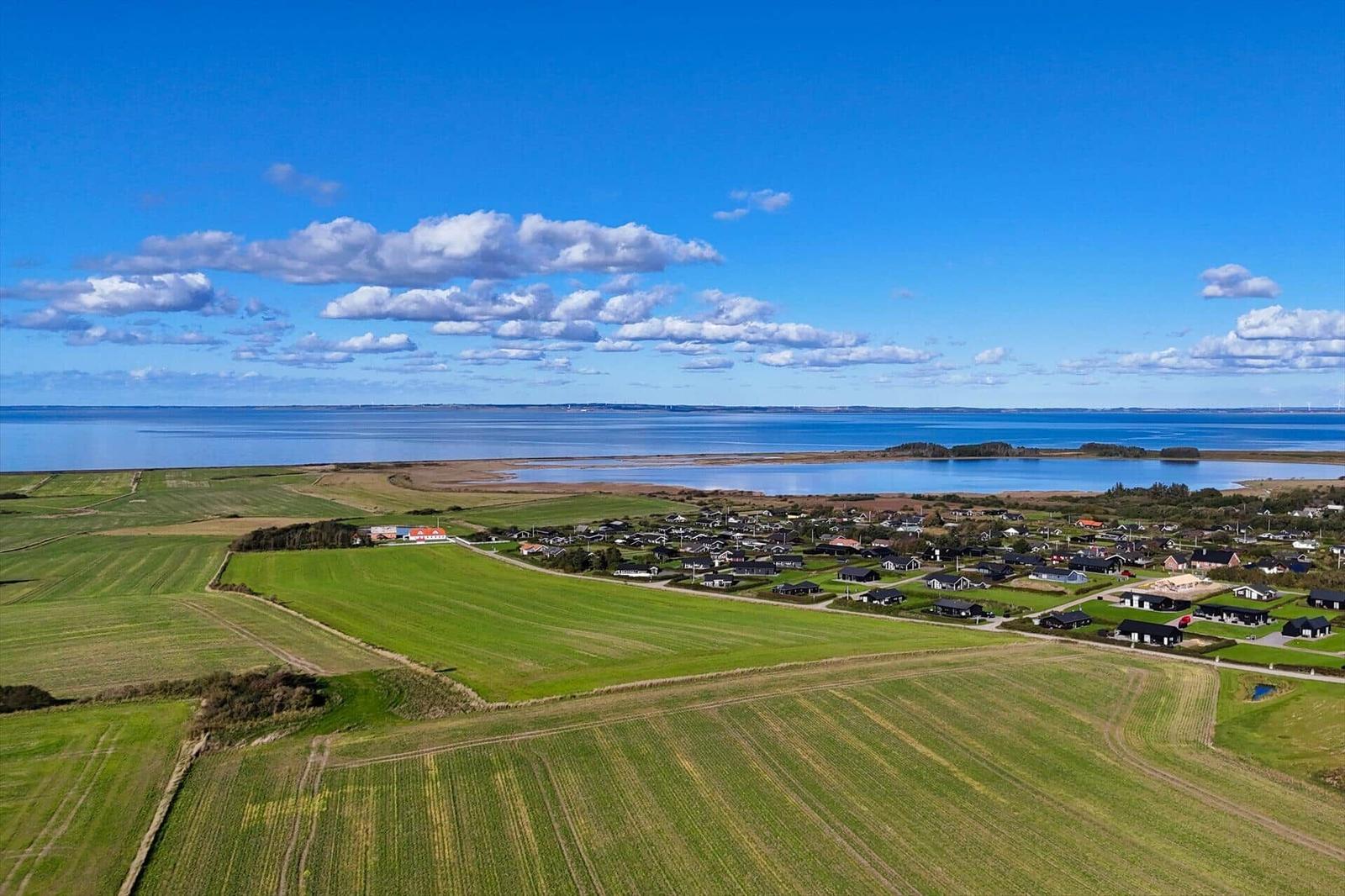 Panorama über Felder, Häuser und Meer unter blauem Himmel mit weißen Wolken.