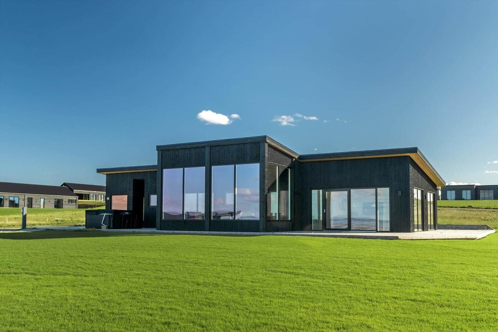 Moderne Villa mit großzügigen Fenstern und grünem Rasen vor einem klaren Himmel.