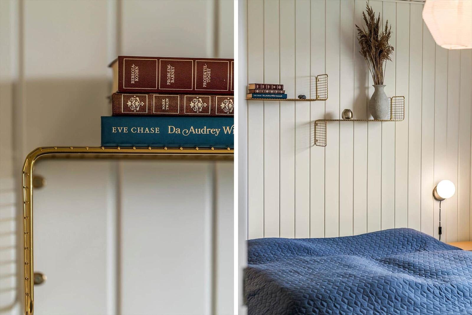 Schlafzimmer mit blauer Bettdecke, goldener Wandregal und Bücherstapel.