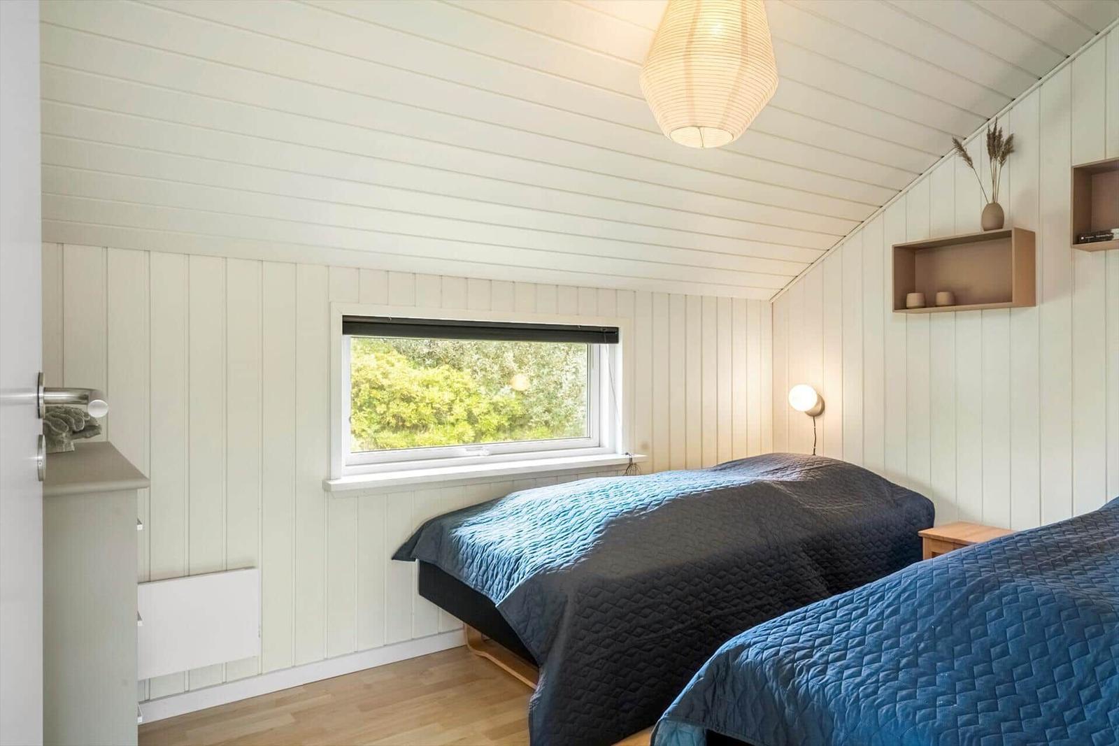 Zwei Betten mit blauen Decken, Fenster mit Blick auf Grün, weiße Wände und Holzboden.