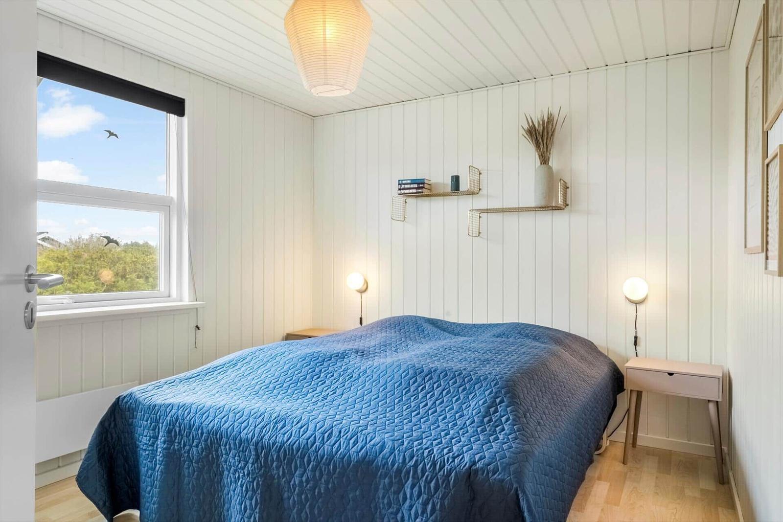 Schlafzimmer mit blauem Bett, Fenster und Wandregalen.