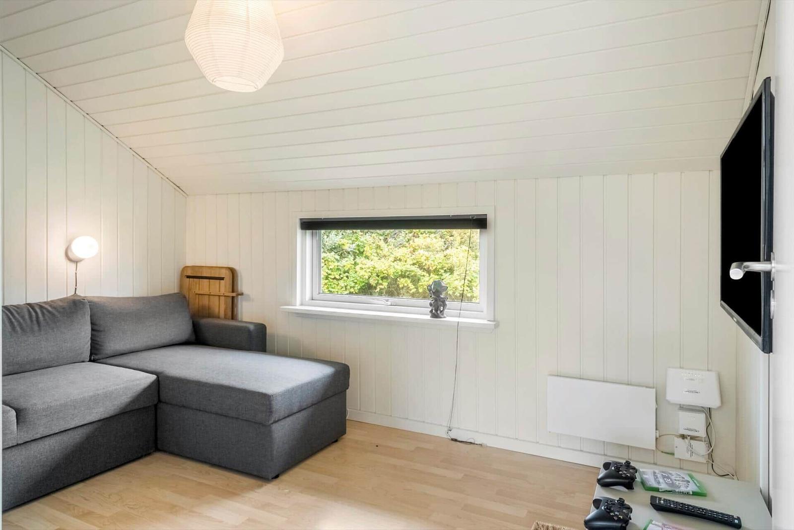 Ein Wohnzimmer mit grasem Sofa, Fenster und Fernseher an der Wand.