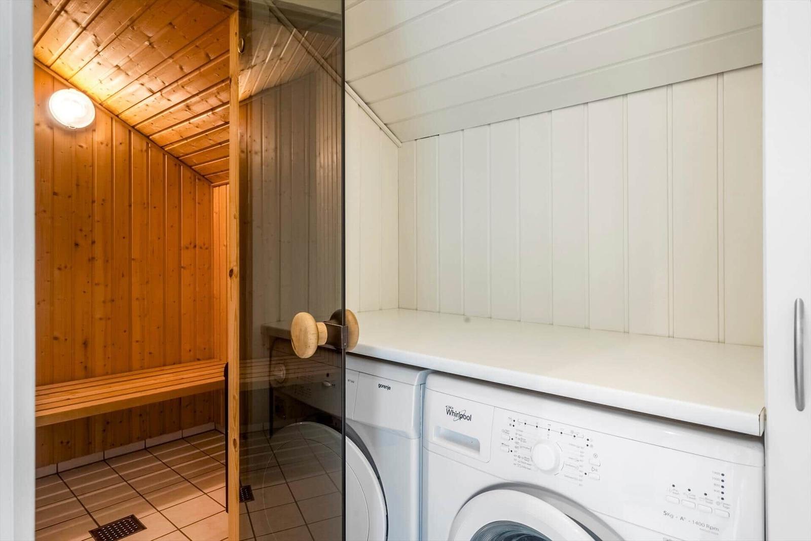 Waschmaschine und Trockner neben einer Sauna mit Holzwand und Bank.