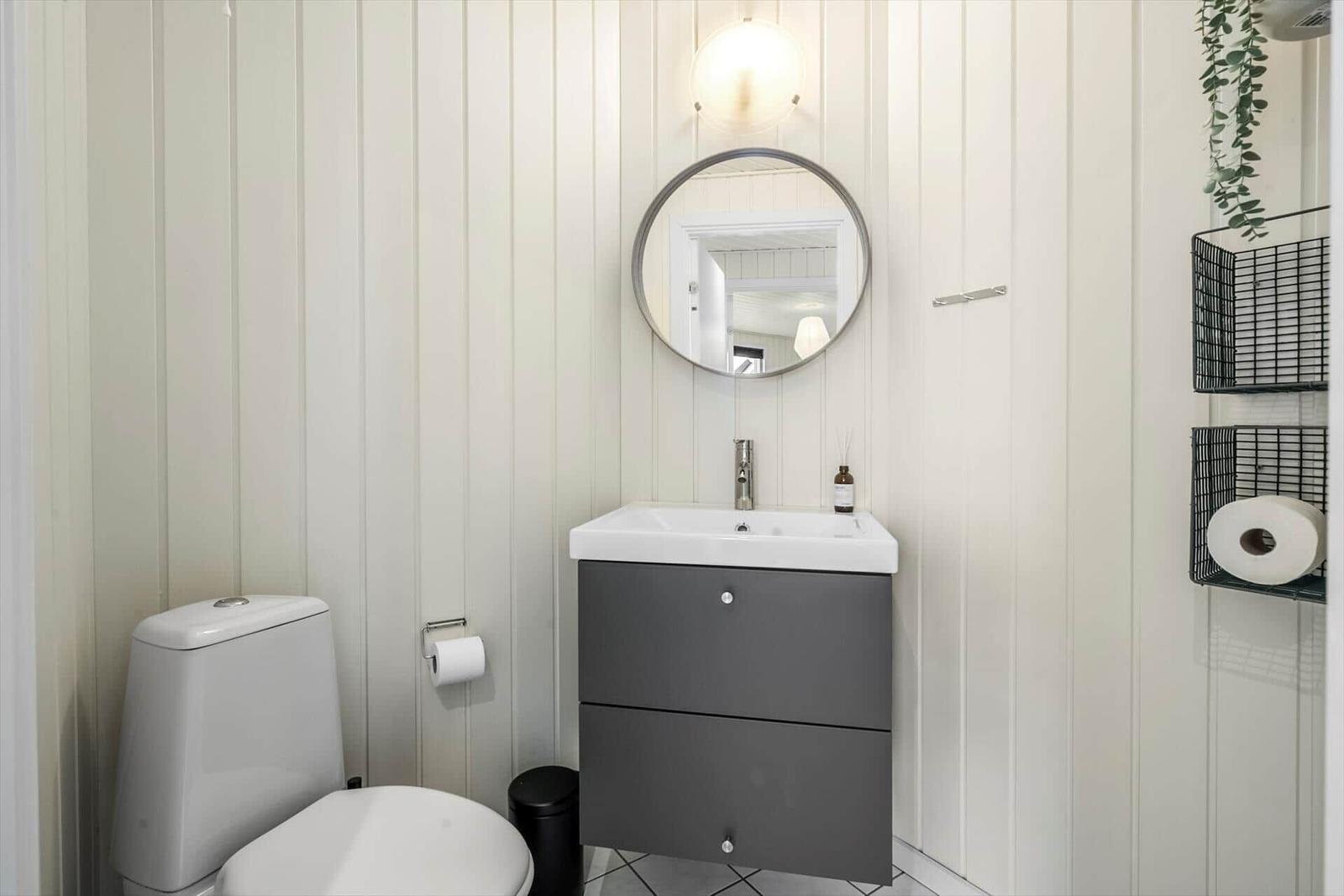 Badezimmer mit Toilette, Waschbecken und Spiegel an vertikal verkleideten Wänden.