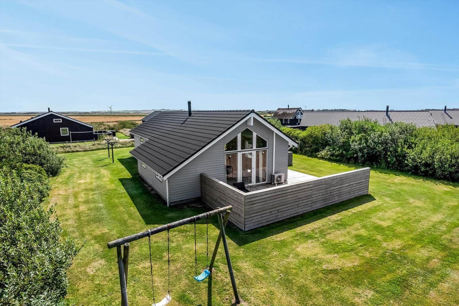 Moderne Holzhütte mit Terrasse und Spielplatz auf grünem Grundstück.
