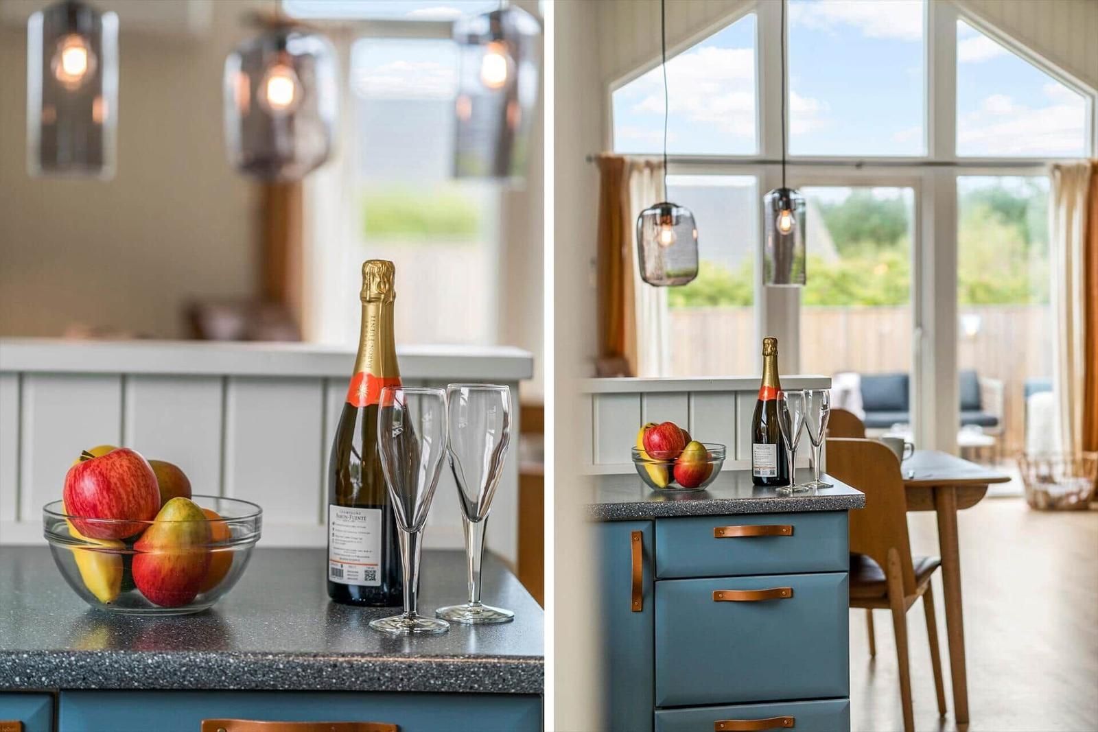 Küchenbereich mit Obstschale, Sekt und Gläsern. Große Fenster mit Blick auf Garten.