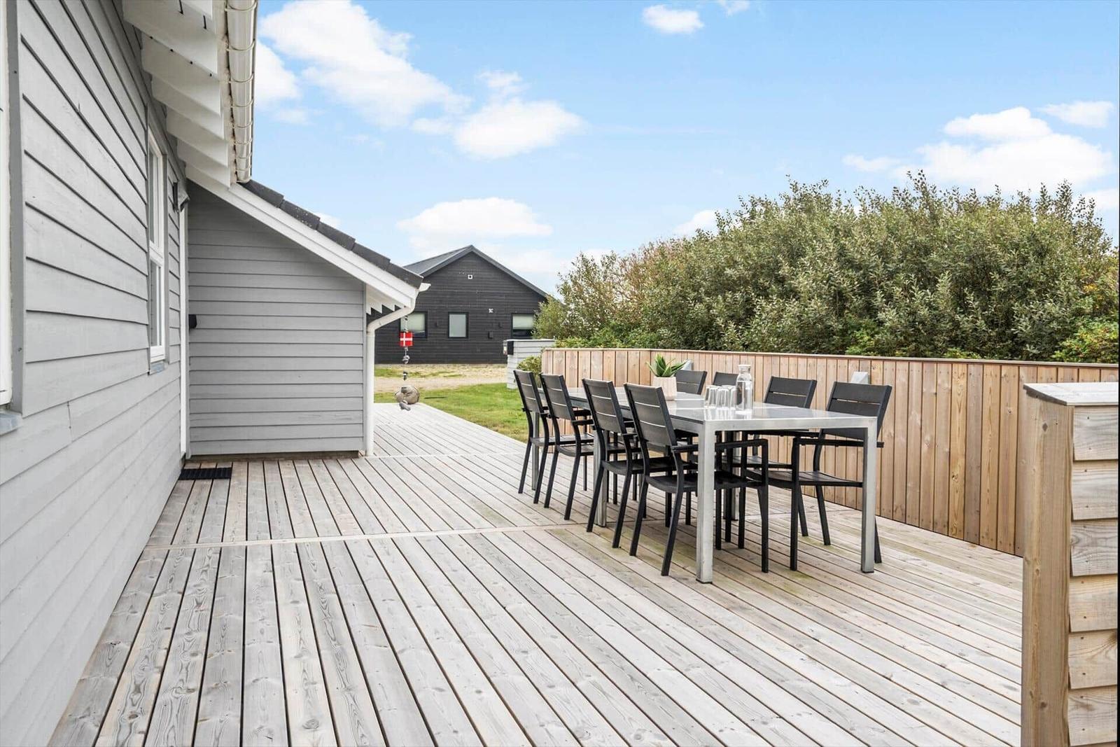 Terrasse mit Esstisch und Stühlen, Holzdecke und Gartenzaun im Hintergrund.