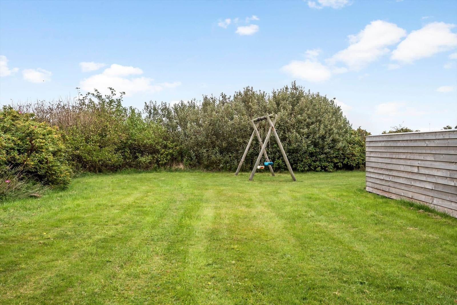 Grüner Garten mit Schaukel und Hecke. Holzwand rechts.