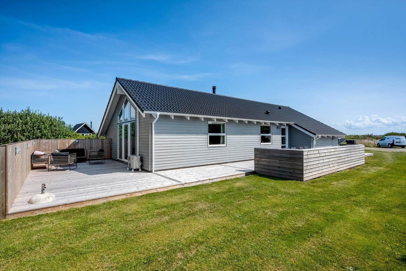 Moderne Villa mit Holzterrasse und Garten. Außenbereich mit Sitzgelegenheiten.