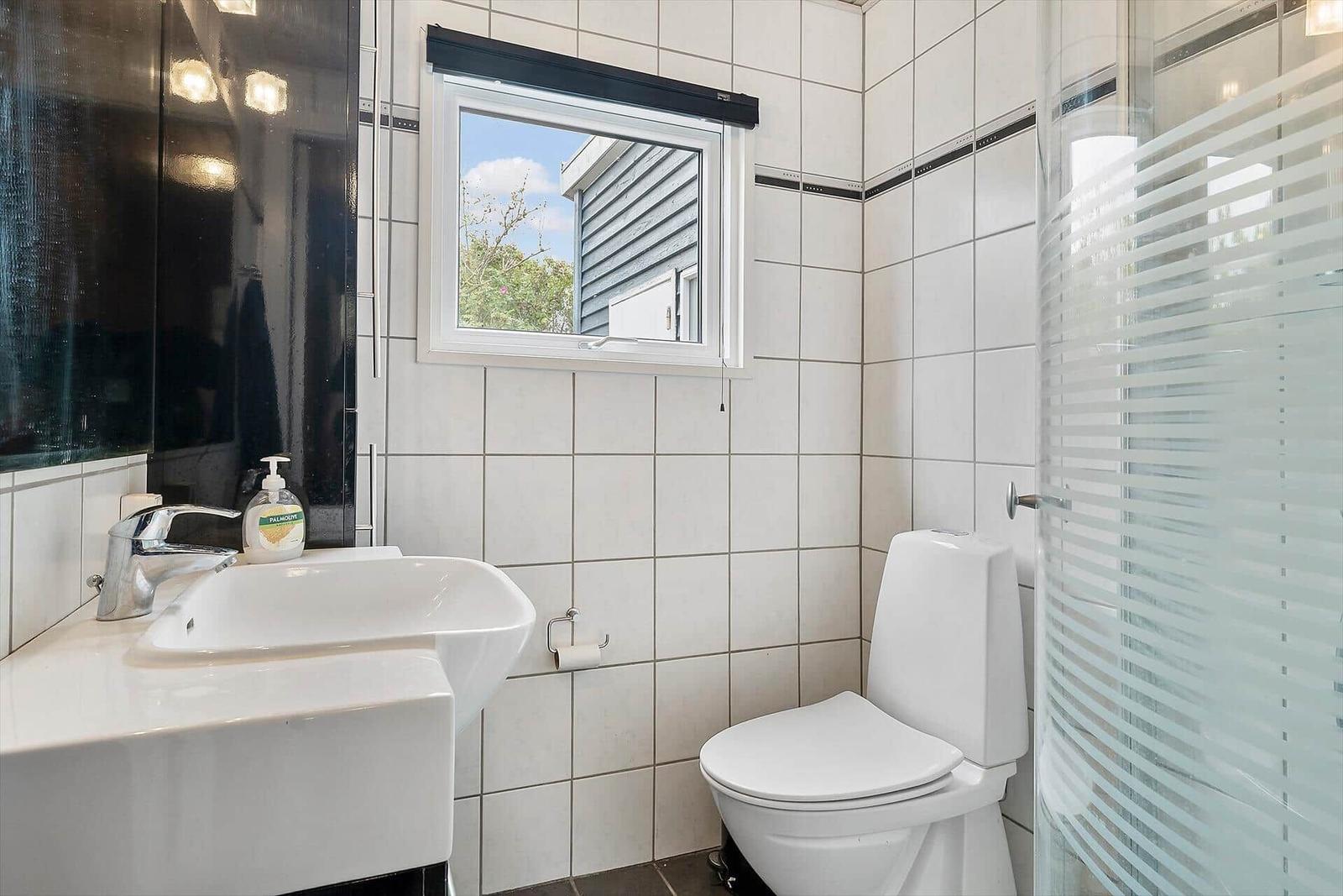 Badezimmer mit Toilette, Waschbecken und Dusche. Fenster mit Blick nach draußen.