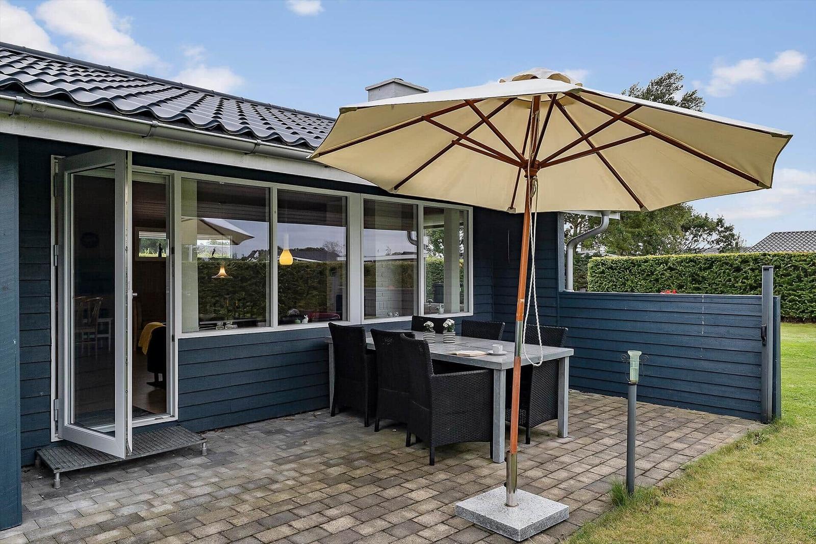 Terrasse mit Tisch, Stühlen und Sonnenschirm. Glastür führt ins Haus. Hinterhof mit Hecke.
