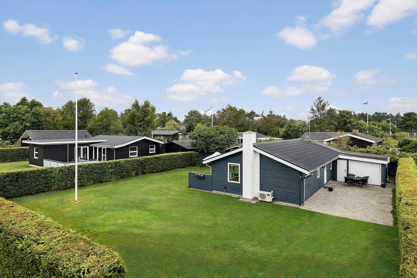 Modernes Ferienhaus mit Garten und Terrasse unter blauem Himmel.