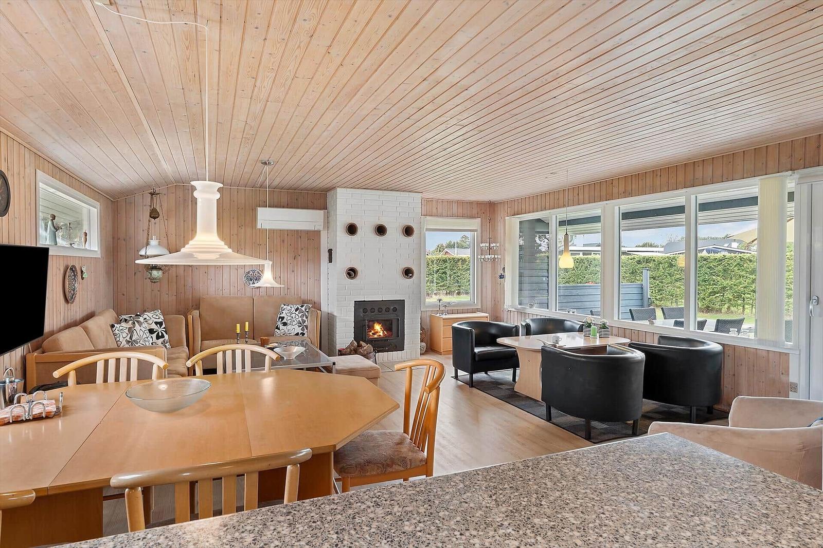 Wohn- und Essbereich mit Kamin, Holzdecke und großen Fenstern.