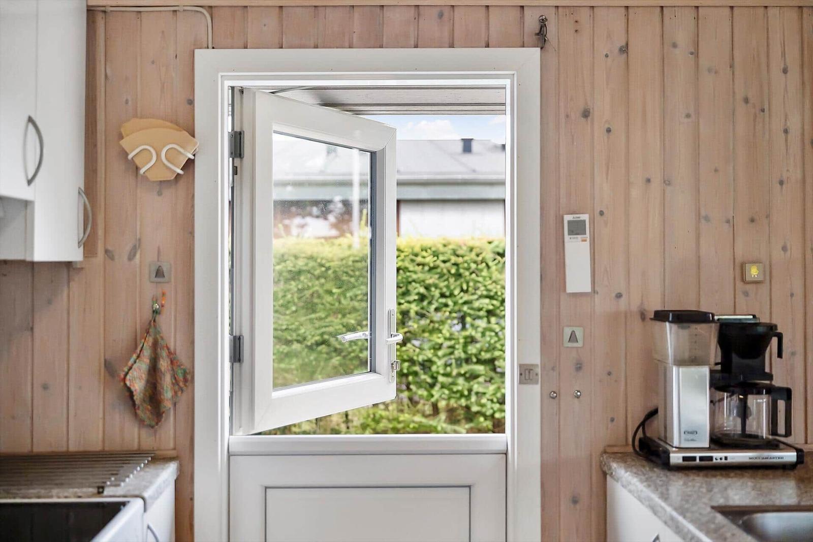 Küche mit Holzwand, geöffnetem Fenster und Kaffeemaschine.