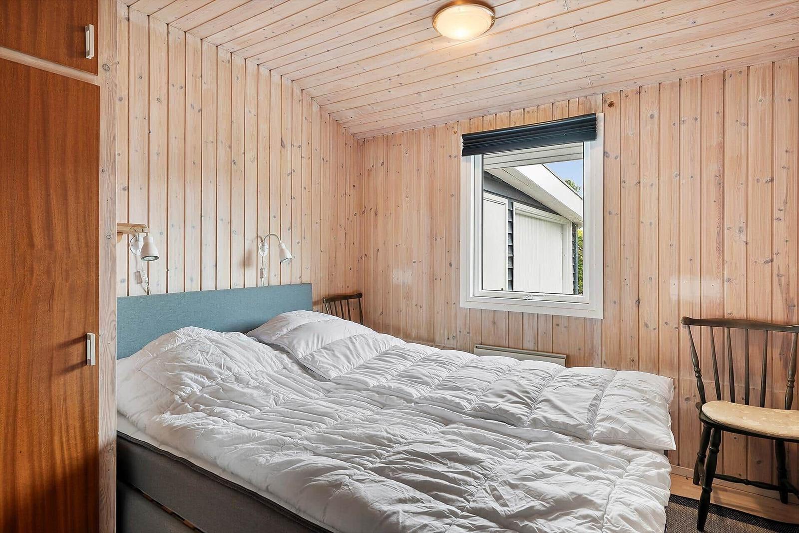 Schlafzimmer mit Holzwand, Bett und Fenster