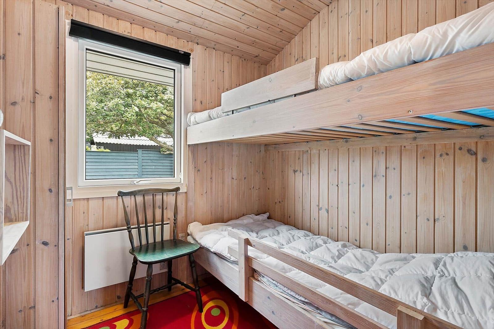 Zimmer mit Doppelstockbett, Holzwand und Fenster mit Blick auf Grün.
