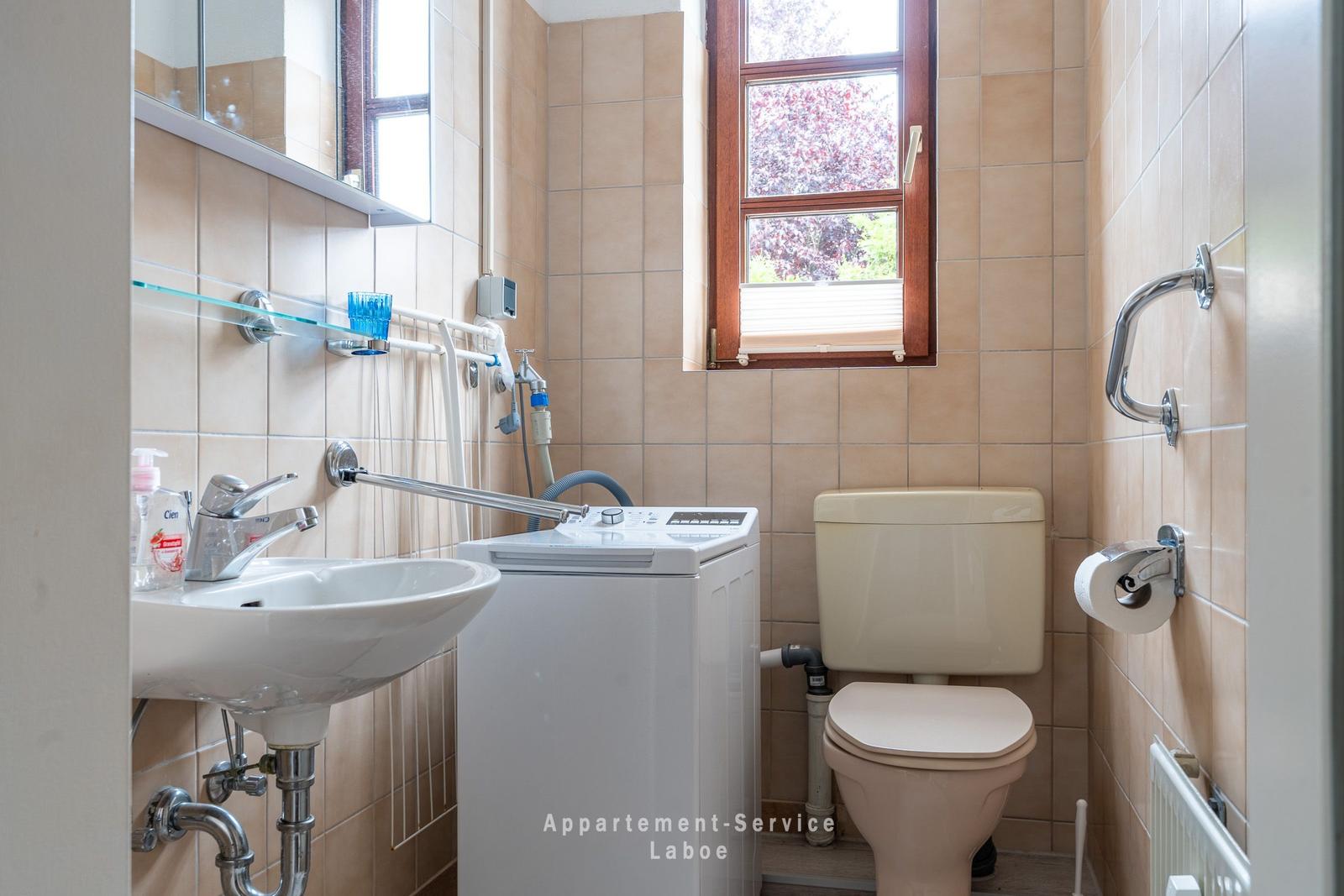 Badezimmer mit Waschmaschine, Toilette und Fenster.