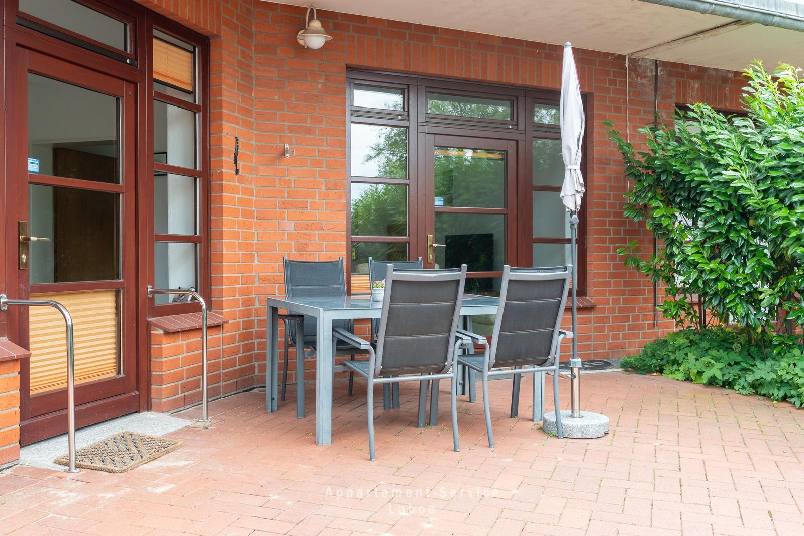 Terrasse mit Tisch, Stühlen und Sonnenschirm neben rotem Backsteinhaus
