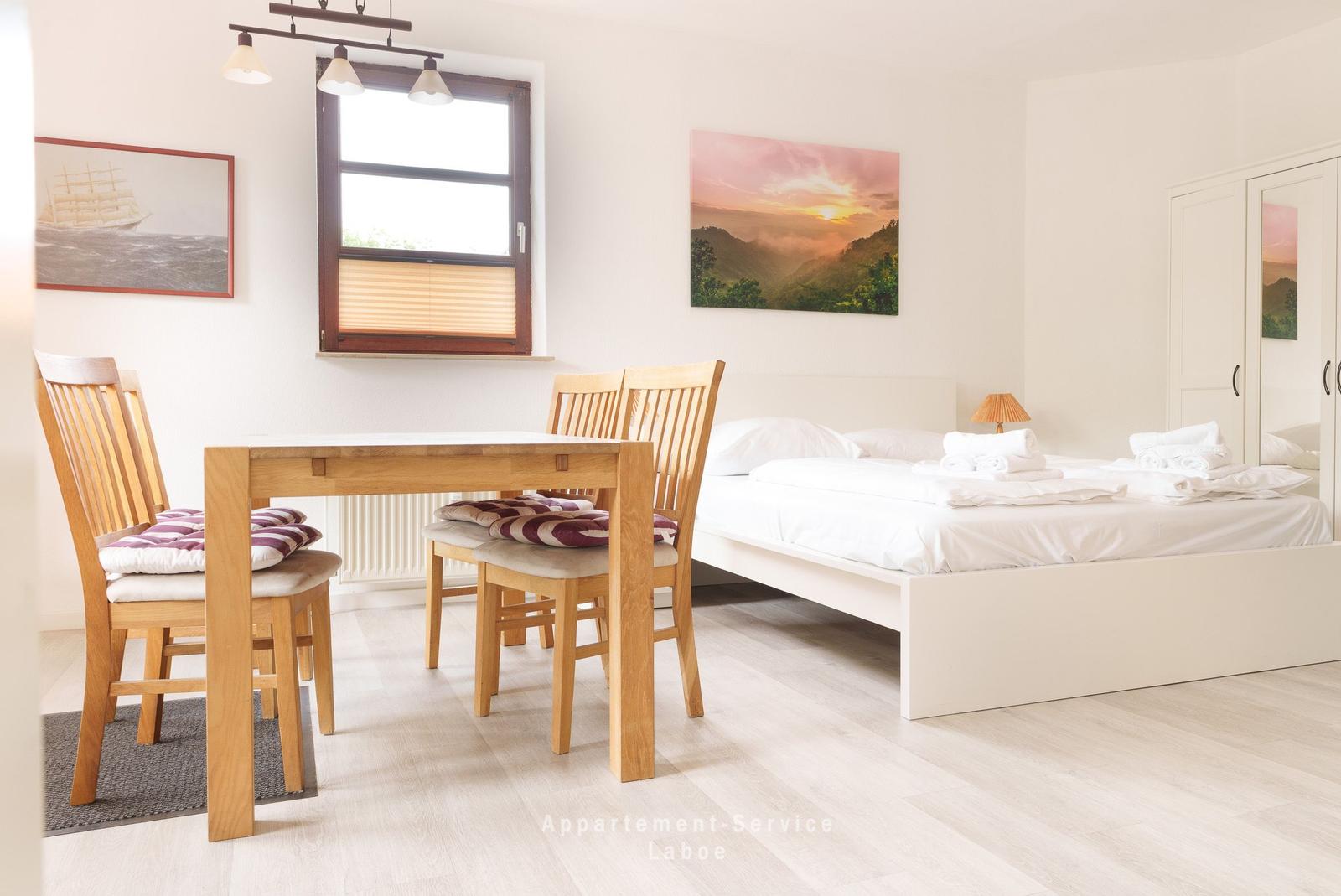 Schlafzimmer mit Bett, Tisch und Stühlen, Fenster und Wandbild.