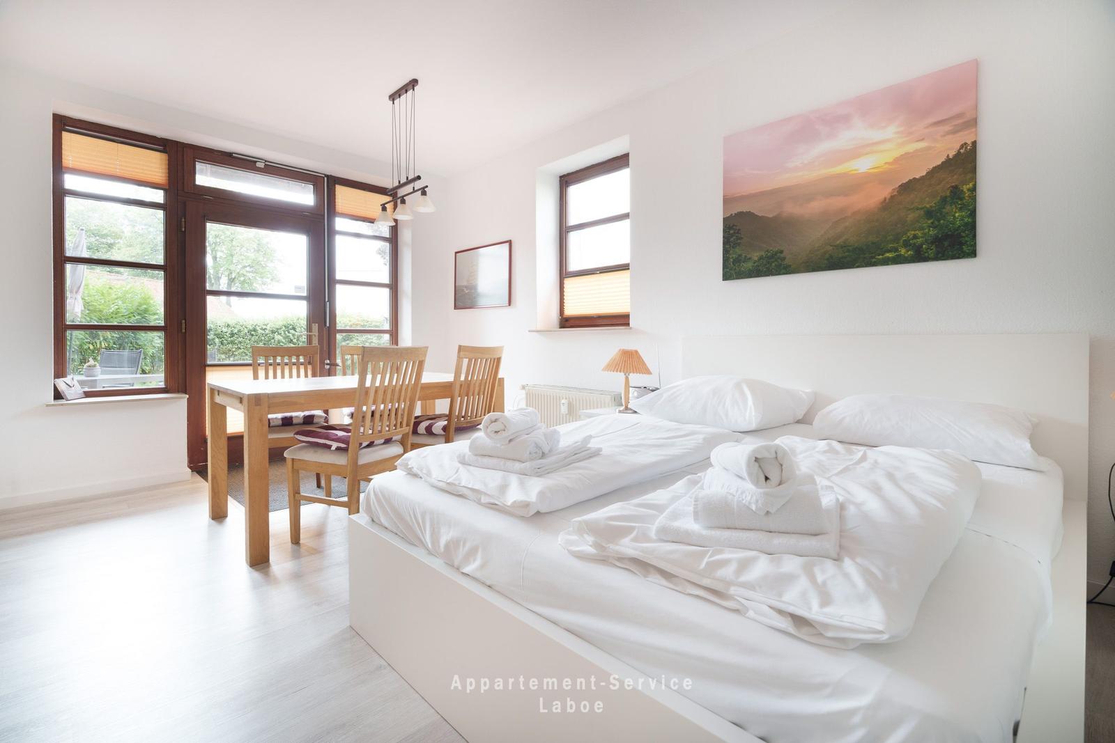 Ein Schlafzimmer mit Bett, Esstisch und Fenster zur Außenterrasse.