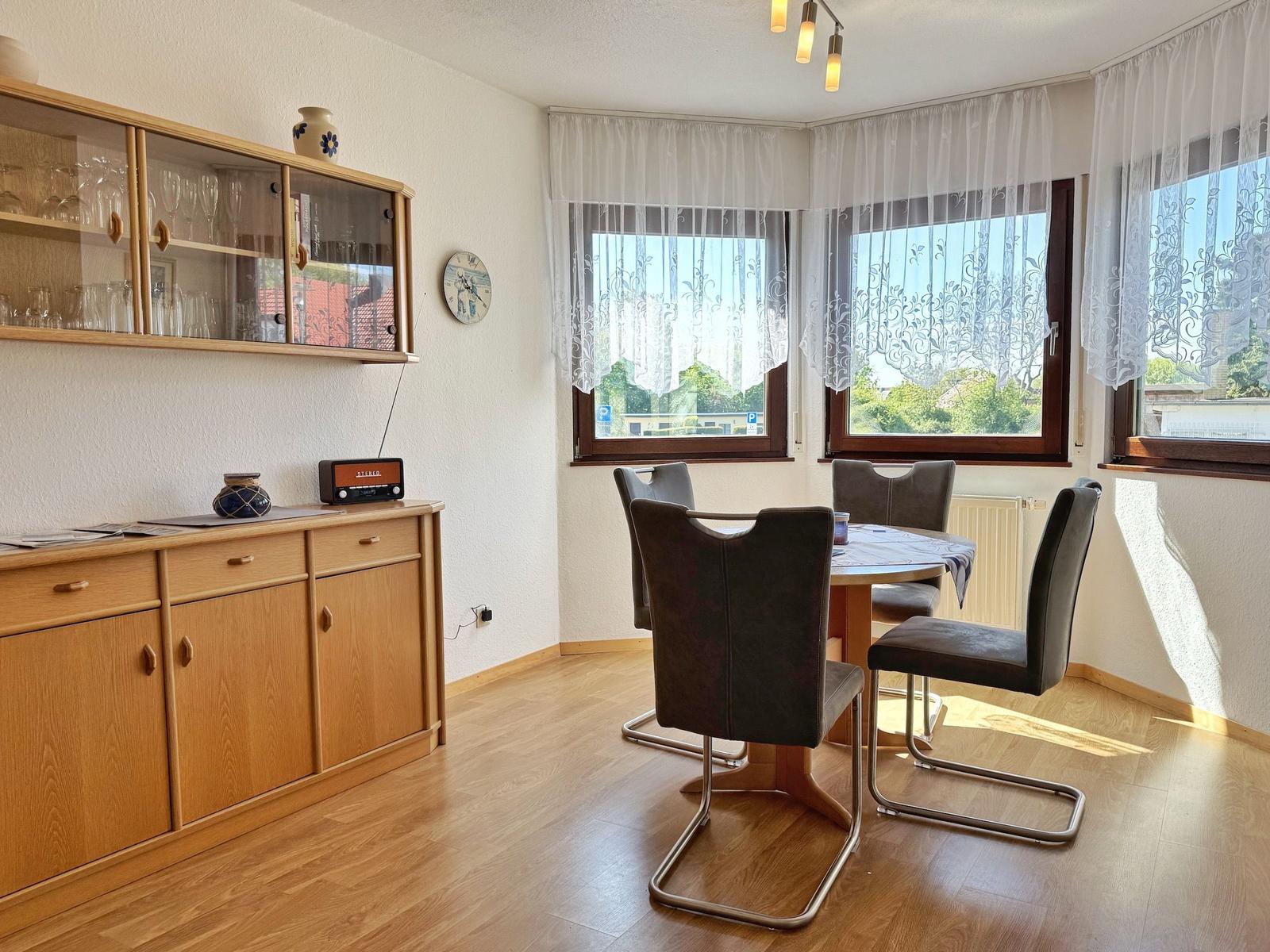 Esszimmer mit Tisch, Stühlen, Fenstern und Holzmöbeln.