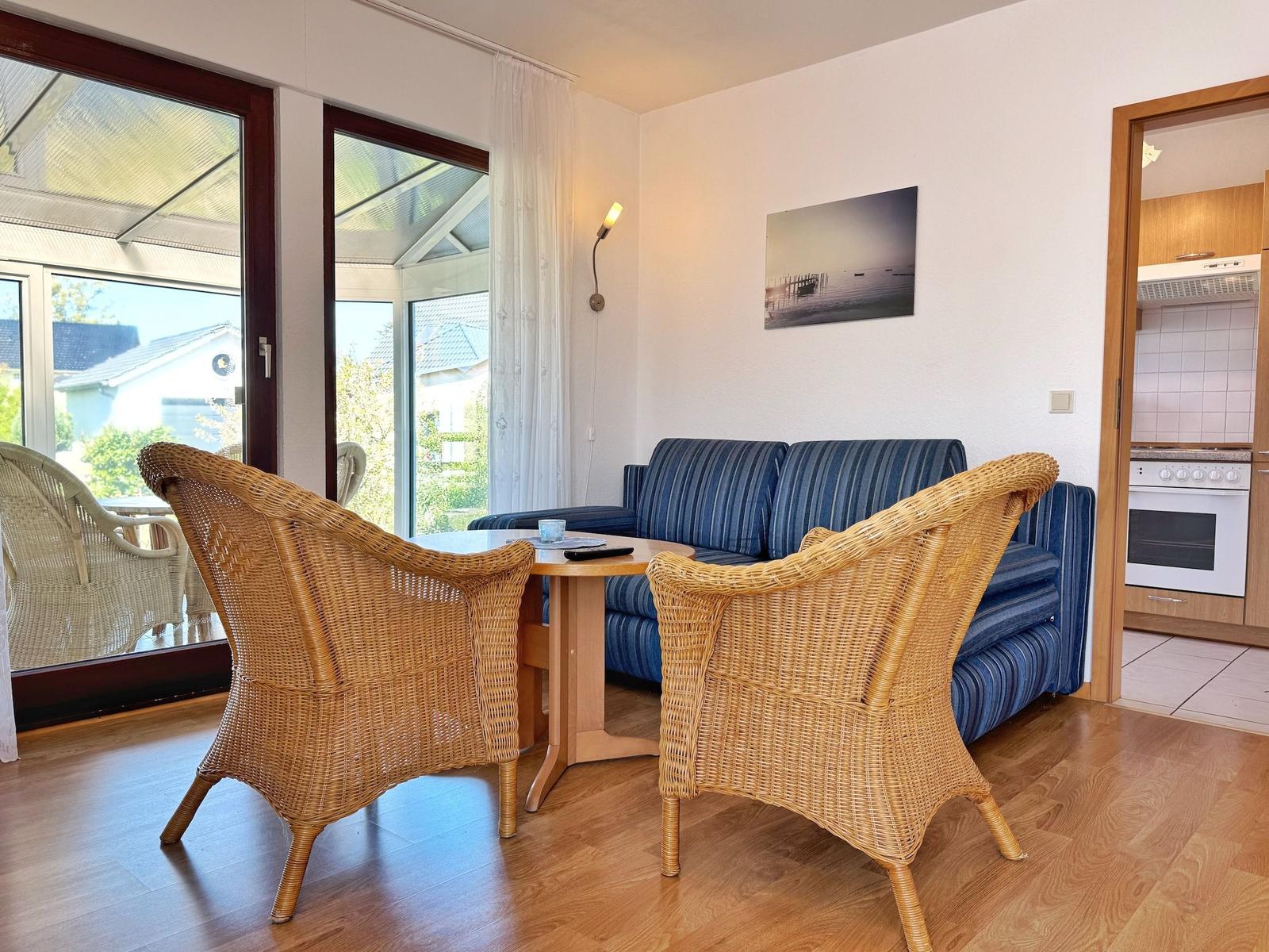 Wohnzimmer mit Sofa, zwei Rattanchairs und Blick auf Terrasse.