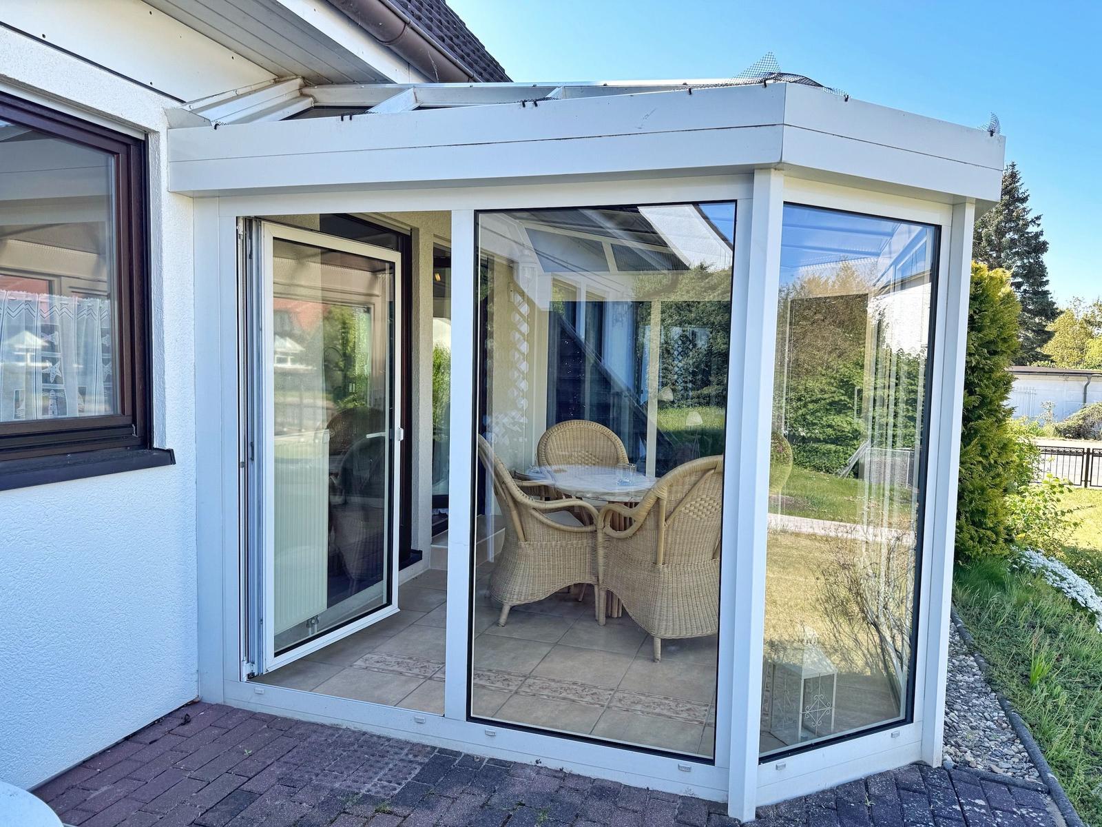 Glasveranda mit Sitzgruppe und Terrassenzugang.