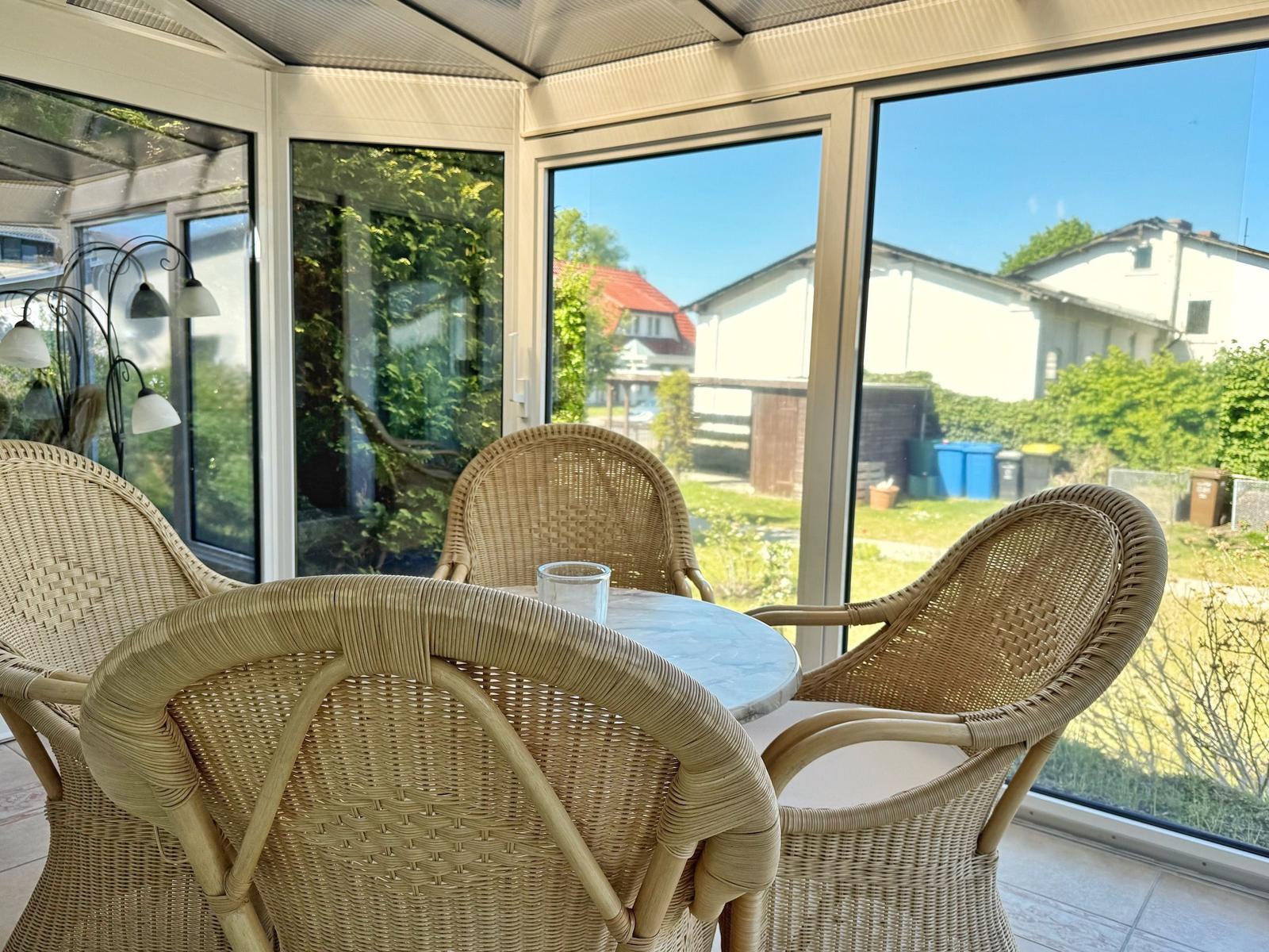 Terrassentisch mit drei Stühlen unter Glasdach. Blick auf Garten und Nachbarhäuser.