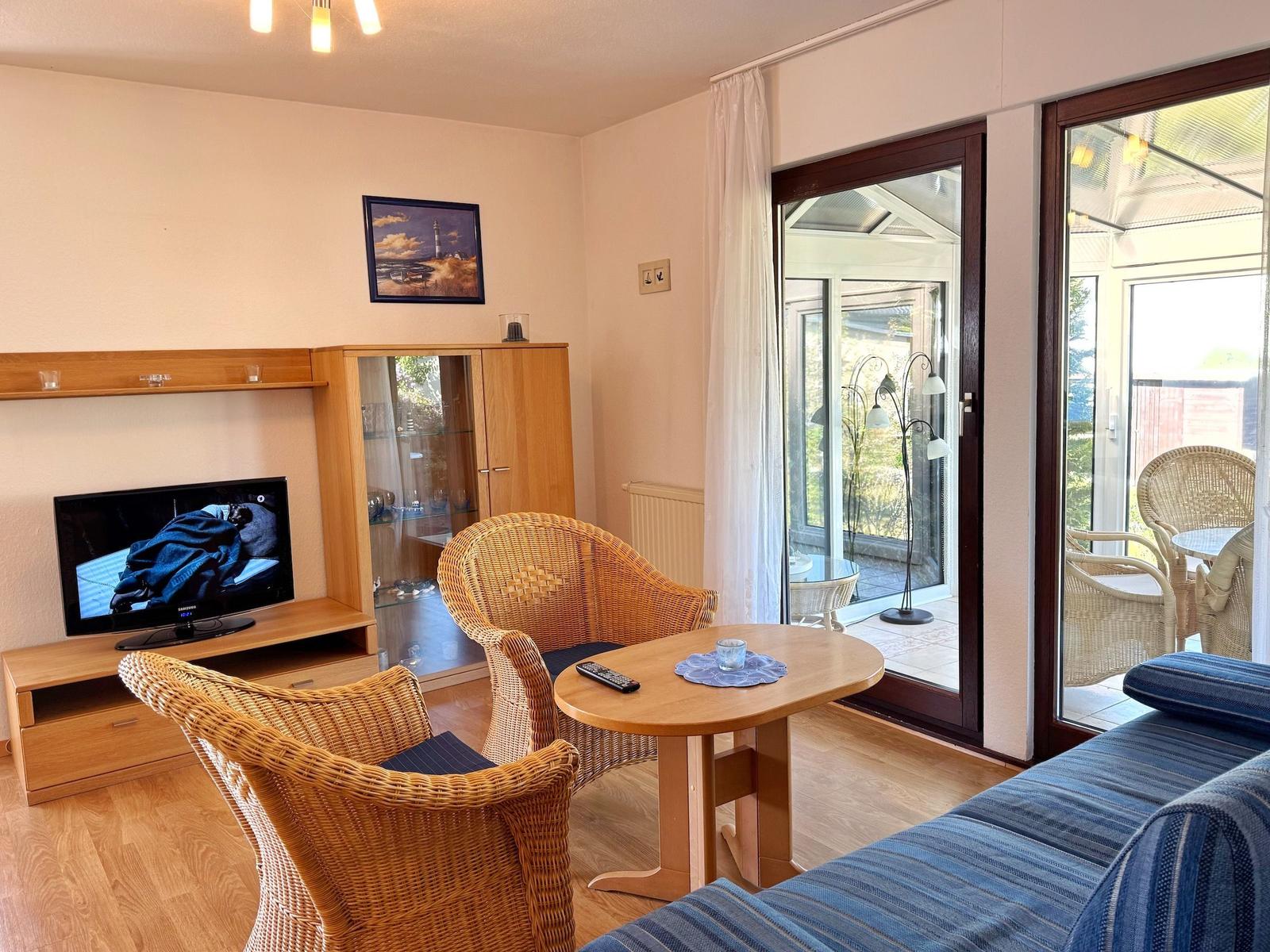 Wohnzimmer mit TV, Sitzgelegenheiten und Zugang zur Terrasse.