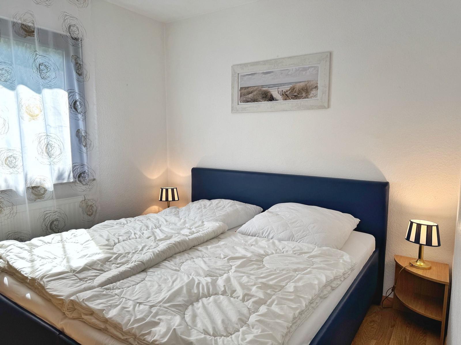 Schlafzimmer mit Doppelbett, zwei Nachttischen und Wandbild.