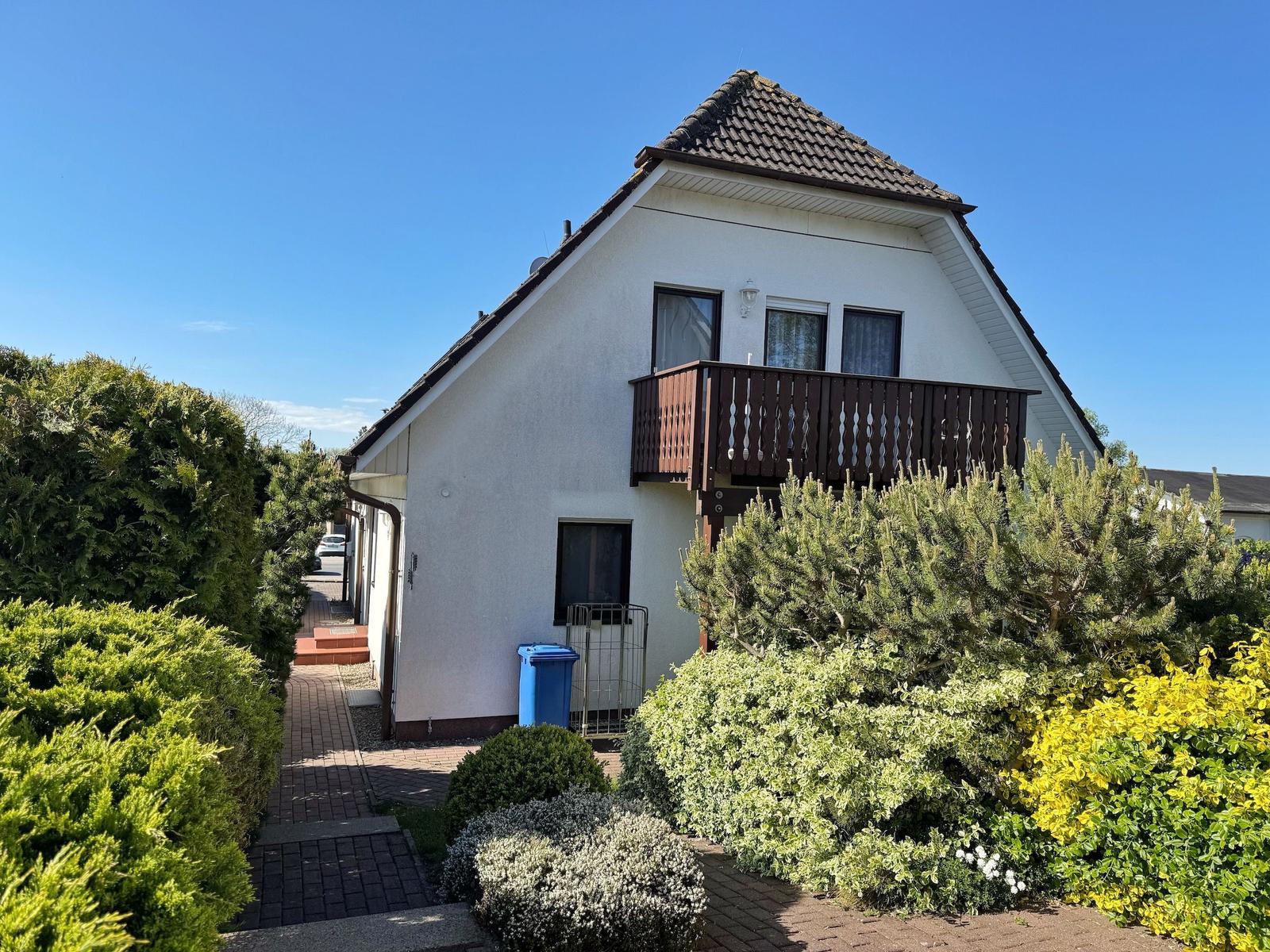 Haus mit Balkon, gepflegtem Garten und blauem Mülleimer.
