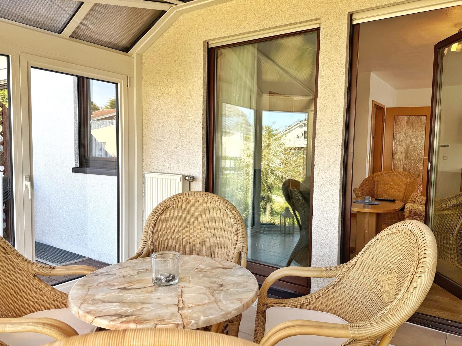 Terrasse mit Rattanstühlen und Marmor-Tisch. Durchgehendes Glas zur Wohnung.