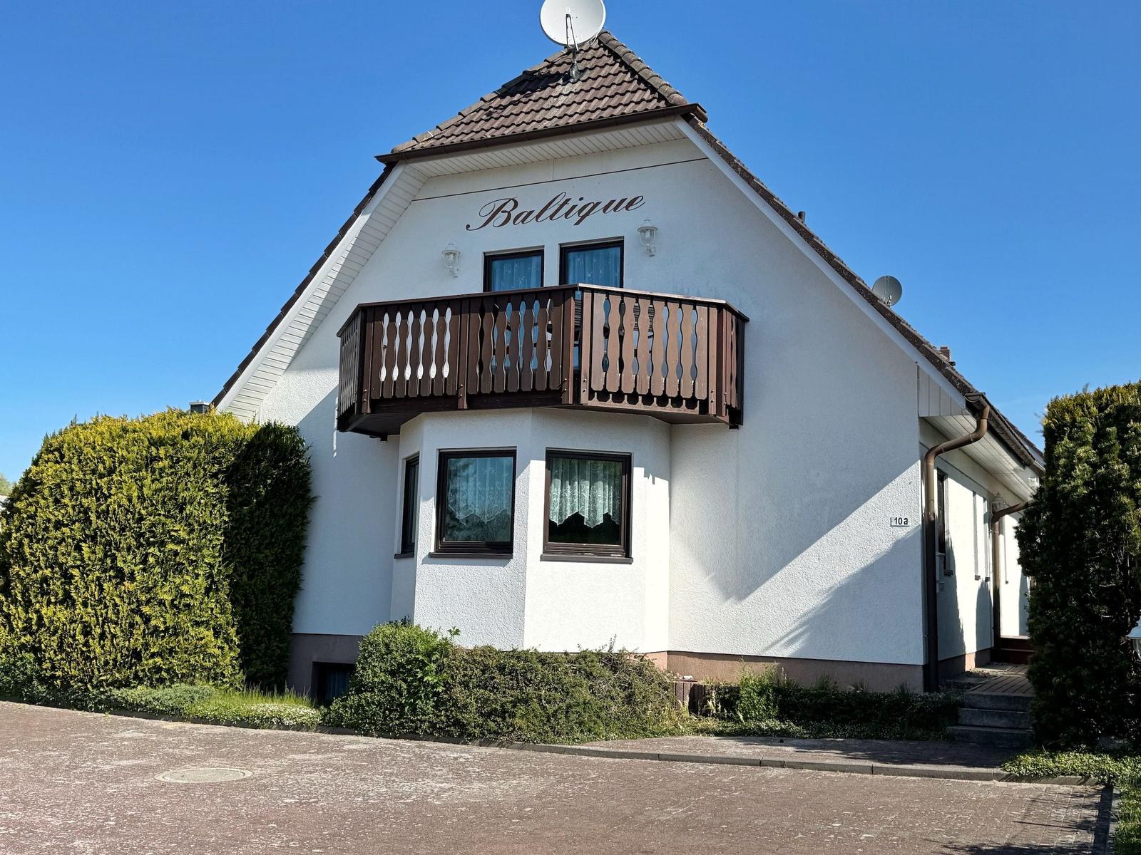 Wohnhaus mit Balkon, weißen Wänden und Satellitenschüssel unter blauem Himmel.