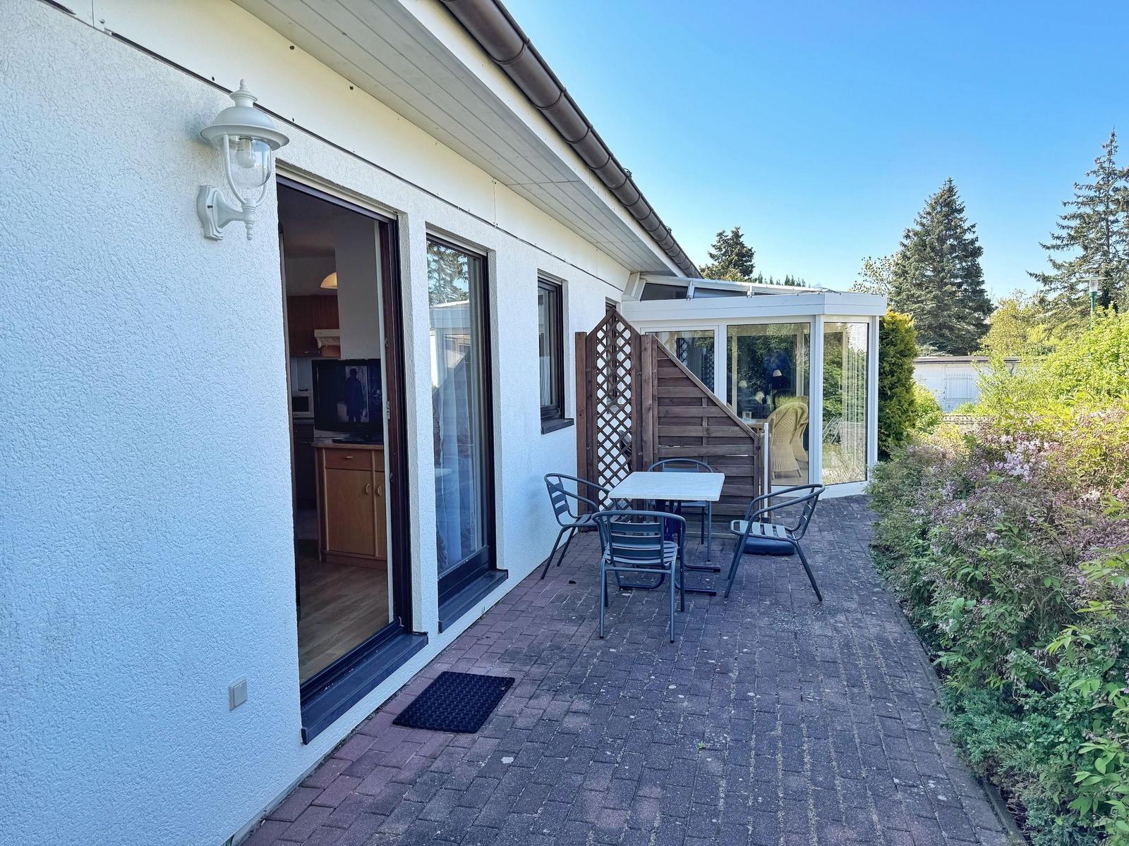 Terrasse mit Tisch und Stühlen neben Haus mit Glasveranda.