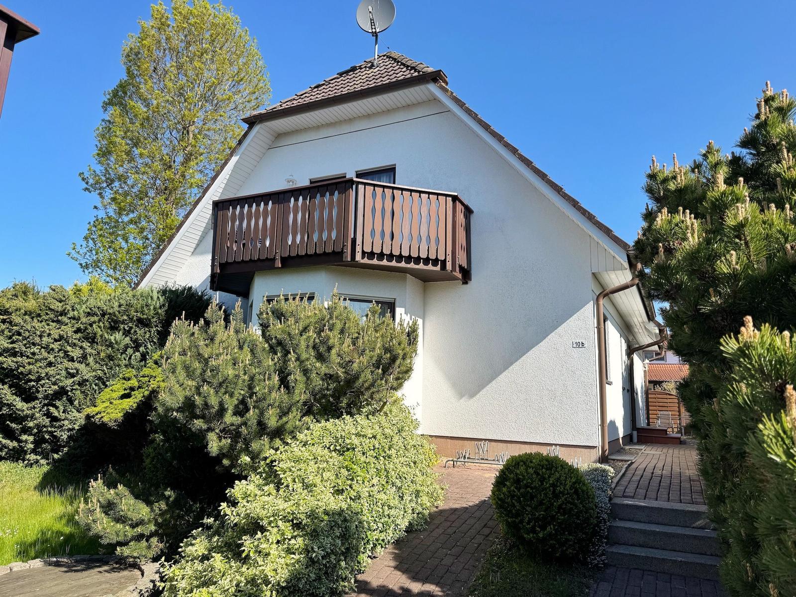 Wohnhaus mit Balkon, Garten und gepflastertem Weg unter blauem Himmel.