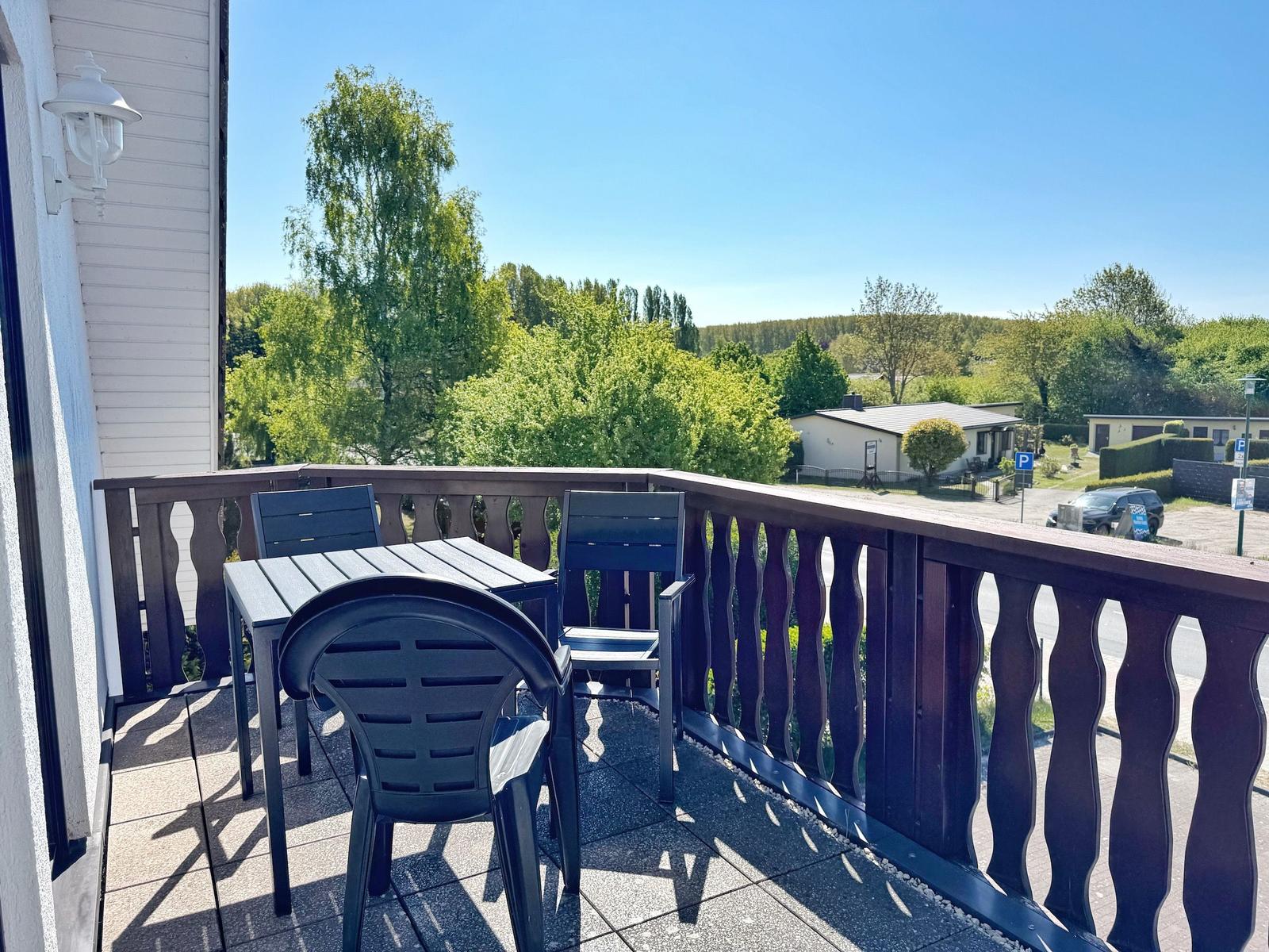 Terrasse mit Tisch und Stühlen, Blick auf grüne Bäume und Wohnhäuser.