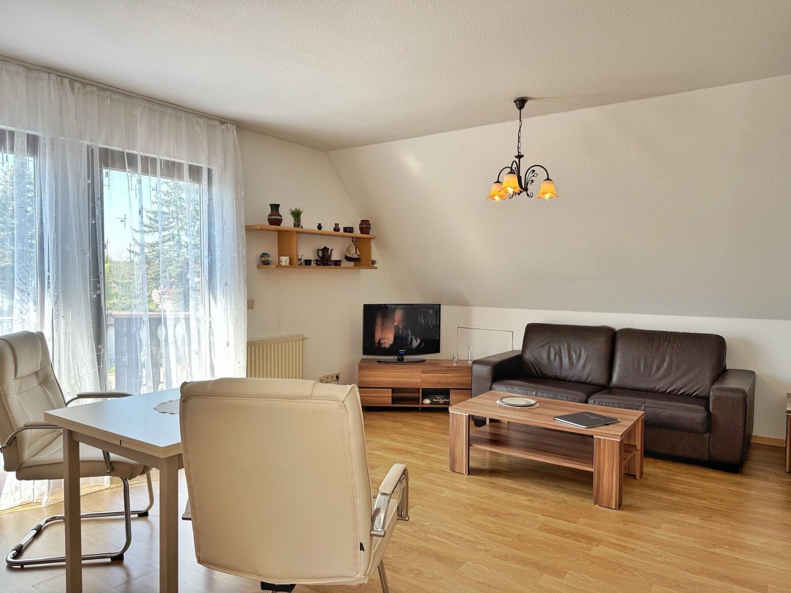 Wohnzimmer mit Sofa, TV und Essbereich. Holzboden und große Fenster.